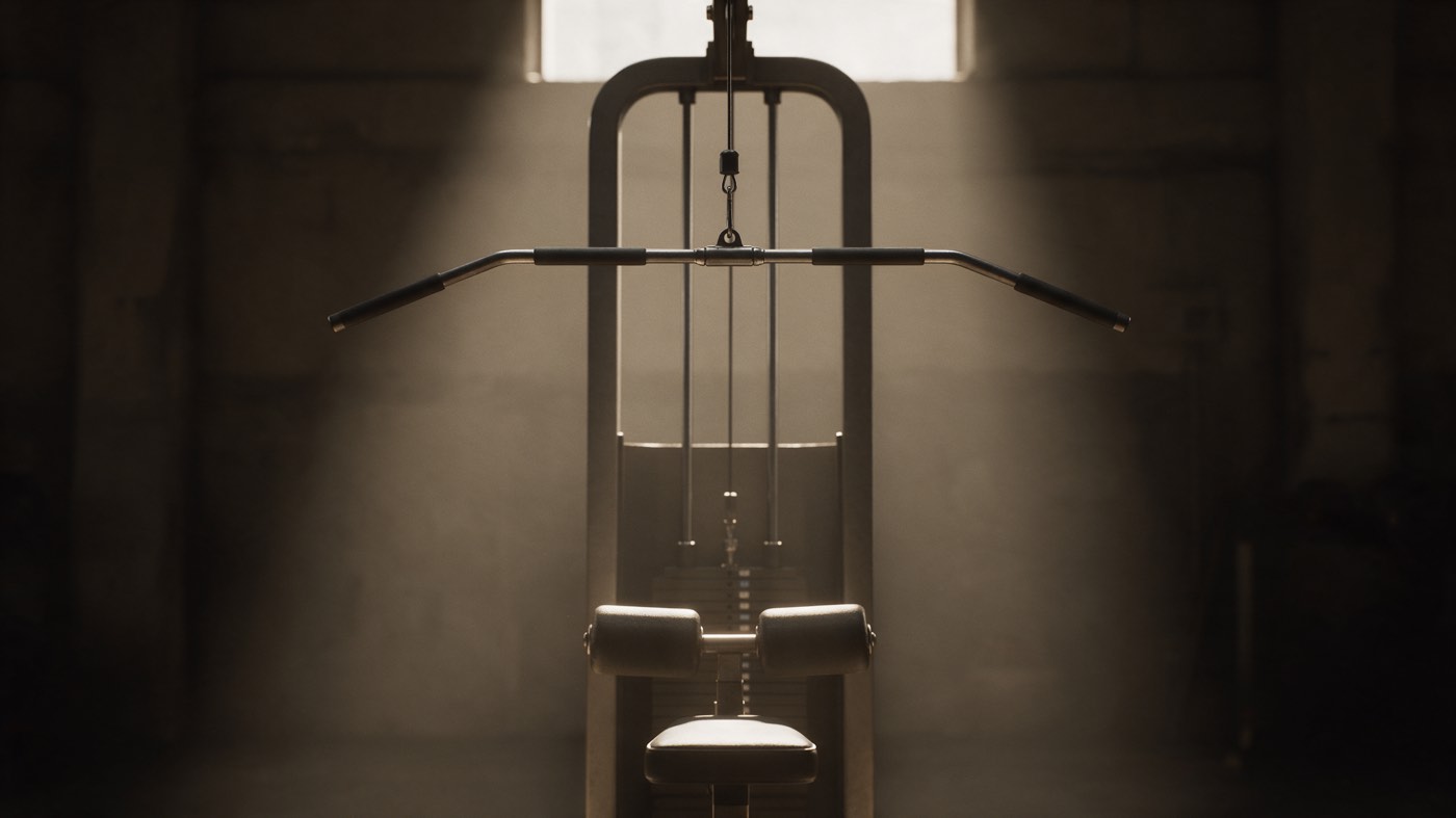 A lat pulldown tower seen head-on: a wide bar hanging from the cable above an empty seat with thigh pads, the weight stack behind it, backlit by a window